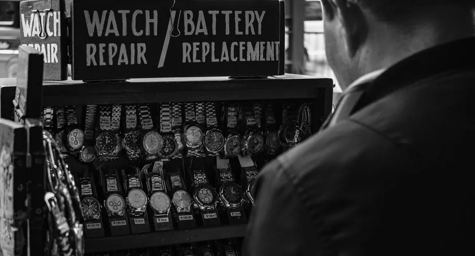 Monochrome image of a watch repair stand with various wristwatches and signage.